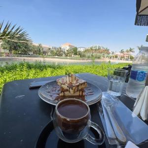 Madinaty Luxury Apartments New cairo في Madinaty: كوب من القهوة وكعكة على طاولة