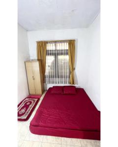 Cama roja en habitación con ventana en Berkah Huni , CIATER, en Sarireja