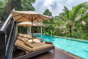 a poolside deck with lounge chairs and an umbrella at The Hidden Palace by Hanging Gardens in Payangan
