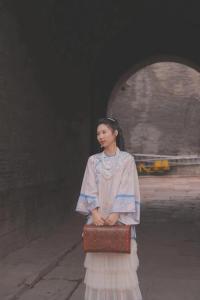 una mujer con un vestido sosteniendo una maleta en Pingyao hu lu wa Home Inn, en Pingyao