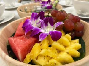 DM Hotel & Cafe في Ban Na Tho: وعاء من الفاكهة مع الزهور الأرجوانية والعنب