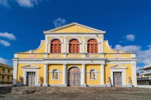 un bâtiment jaune avec des fenêtres rouges et un ciel bleu dans l'établissement Cyrus appartements, à Pointe-à-Pitre