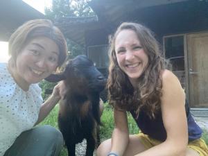dos mujeres sentadas al lado de una cabra bebé en Kizuna Guesthouse, 
