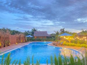 a swimming pool with two picnic tables and umbrellas at Mekong Silt Ecolodge - Swimming Pool & Free Breakfast in Can Tho