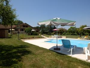 a swimming pool with an umbrella and chairs and a table and an umbrella at Gîtes Perruchet in Castelnavet