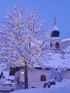 un árbol cubierto de nieve con luces frente a un edificio en Jochum Hotel Garni, en Fiss