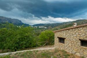 un edificio de piedra con montañas en el fondo en Casa Rural Ca Ferminet & Cabañas de montaña La Garriga, en Benisili