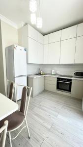 een keuken met witte kasten, een tafel en een koelkast bij " Для Вас "- ЖК 4 Yои 2-х комнатная in Alma-Ata
