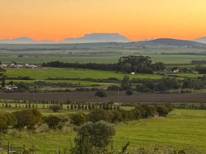 pomarańczowy zachód słońca nad zielonym polem z górami w tle w obiekcie Black Pearl Wine Cottage w mieście Suider-Paarl