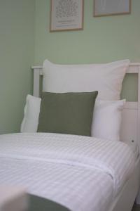 1 cama con sábanas blancas y almohada verde en 80 m2 l Central lWLAN lNetflix l MuYa Apartments, en Hannover