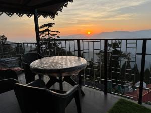 a table and chairs on a balcony with a sunset at Aama Home Stay in Kurseong
