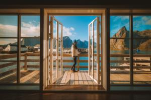 a woman standing on a dock looking out of a window at Reinefjorden Sjøhus in Reine