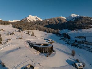 a building in the snow with mountains in the background at Familienhotel Familiamus in Maranza