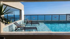 a swimming pool with two chairs and a view of the ocean at Barra Stella do Mar Studio in Salvador