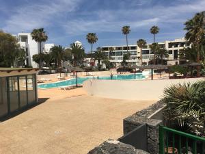 a swimming pool in a resort with palm trees and buildings at Bungalow GOA Pool view, Playa Roca residence sea front access - Free AC - Wifi in Costa Teguise