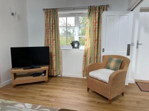 een woonkamer met een televisie en een stoel bij Cottages at Woodlands, Grooms Cottage in Wareham