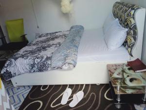 Cama blanca con manta y zapatos en el suelo en Chaka Airbnb. en Nyeri