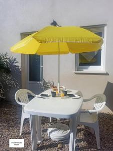 uma mesa branca com um guarda-sol amarelo e duas cadeiras em Studio Quiétude em Saint-Aygulf