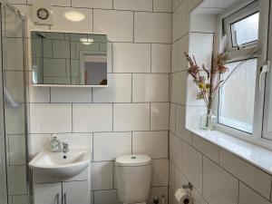 a white tiled bathroom with a toilet and a sink at Kensal Lodge Guest House in London