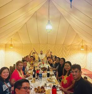 een groep mensen die rond een tafel in een tent zitten bij Luxury Desert Camp Merzouga in Merzouga