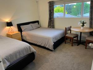 a bedroom with two beds and a table and a window at Hillcrest Homestay, NorthShore, Auckland in Auckland