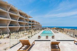 a resort with a swimming pool and chairs and the ocean at Luxurious Ocean View Apartment in Cabo San Lucas