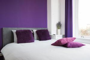 Cama blanca con almohadas moradas y ventana en B&B Slapen bij de burgemeester, en Sint Pancras