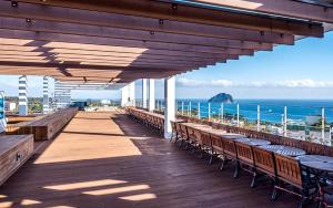 a wooden deck with benches and tables and the ocean at Noblepia Hotel in Seogwipo