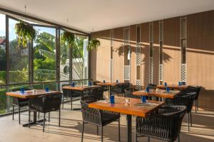 Andaman Beach Hotel Phuket - Handwritten Collection في شاطيء باتونغ: مطعم بطاولات وكراسي ونوافذ كبيرة