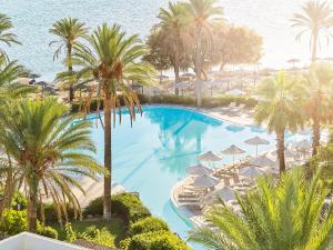 an overhead view of a swimming pool with palm trees and umbrellas at Grecotel Kos Imperial in Kos