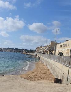 een strand met een hek en het water en de gebouwen bij A day at Dee's in Birżebbuġa
