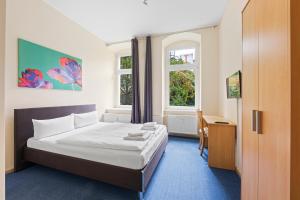 a bedroom with a bed and a desk and two windows at Hotel Comenius in Berlin