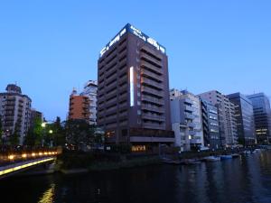 wysoki budynek obok rzeki z budynkami w obiekcie Dormy Inn Tokyo Hatchobori Hot Spring w Tokio