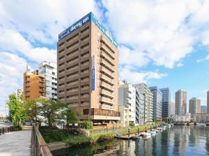 wysoki budynek obok rzeki z budynkami w obiekcie Dormy Inn Tokyo Hatchobori Hot Spring w Tokio