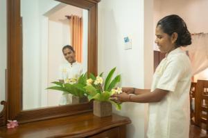 Una donna in piedi davanti a uno specchio con un vaso di fiori di Alai Resort a Mullaittivu