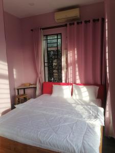 a bedroom with a white bed with pink walls and a window at Jack's Guesthouse in Siem Reap