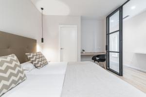 a white bedroom with a large bed and a black chair at Smartr Las Palmas in Las Palmas de Gran Canaria