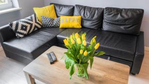 eine schwarze Ledercouch mit einer Vase gelber Tulpen auf einem Tisch in der Unterkunft Apartamenty Szlachecki i Pod Artusem in Danzig