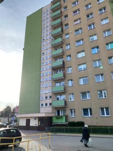 a woman walks past a tall building at Apartament Piechoty Tanie spanie in Elblag