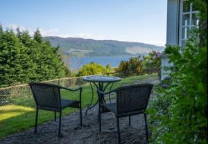 two chairs and a table with a view of the water at Loch Ness Cottages in Brackla