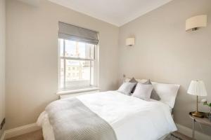 a white bedroom with a white bed and a window at Beaufort Gardens Apartment in Knightsbridge in London