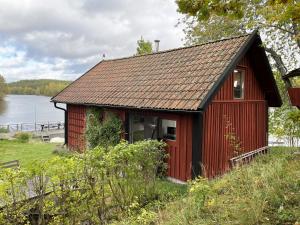 eine rote Hütte an der Seite eines Sees in der Unterkunft Cozy cottage with its own bathing cliff located at Odensvi in Odensvi