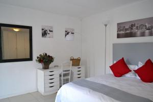 a bedroom with a white bed and a dresser with red pillows at Bryanston Elgin - Cottage 2 in Johannesburg