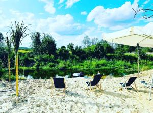 um grupo de cadeiras e um guarda-sol numa praia em Heaven Reset & Spa - Domek nad rzeka em Korczew