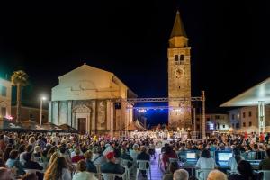 una folla di persone sedute di fronte a un edificio con una torre dell'orologio. di Garden Palace Pool Deluxe Apartment a Umag (Umago) Altre 24 foto