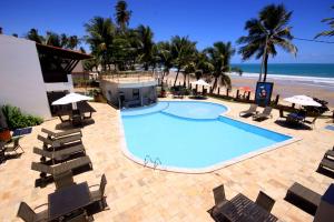 a large swimming pool with chairs and a beach at Pousada Caravelas de Pinzón in Cabo de Santo Agostinho