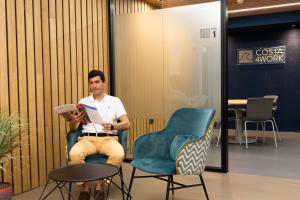 a man sitting in a chair reading a book at RK Farallón Canteras in Las Palmas de Gran Canaria
