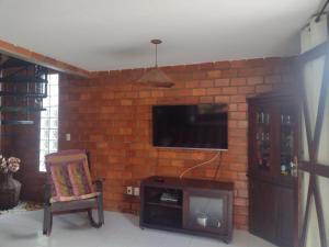a living room with a brick wall with a tv and a chair at Casa 04 do Condomínio Privê Portal das Flores in Gravatá