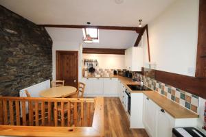 a kitchen with white cabinets and a table and a stone wall at The Hayloft, Broughton Beck, near Ulverston in Spark Bridge