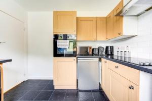 a kitchen with wooden cabinets and a black tile floor at London serviced apartments BAFOG in Barking